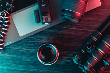 Top view of a desk working with laptop keyboard, modern camera, lens, tripod and a black pen on a wood background. Freelance, creative or online education concept Top view of a desk working with laptop keyboard, modern camera, lens, tripod and a black pen on a wood background. Freelance, creative or online education concept